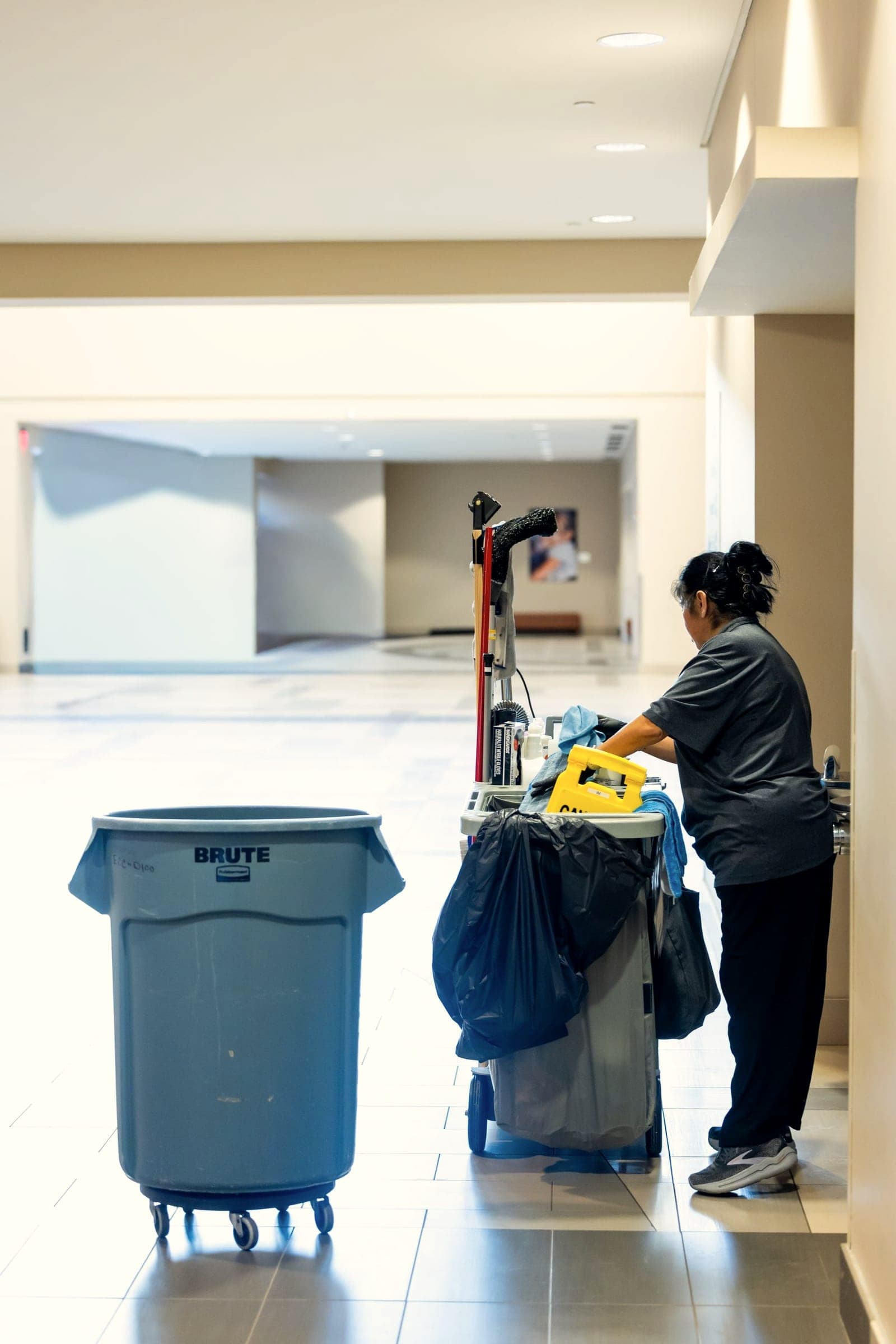 Profissional de limpeza com carrinho de materiais em corredor comercial